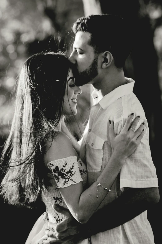 a man kissing the forehead of a woman in a park