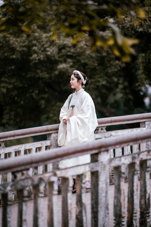 a woman in a white dress and head scarf is standing on a bridge