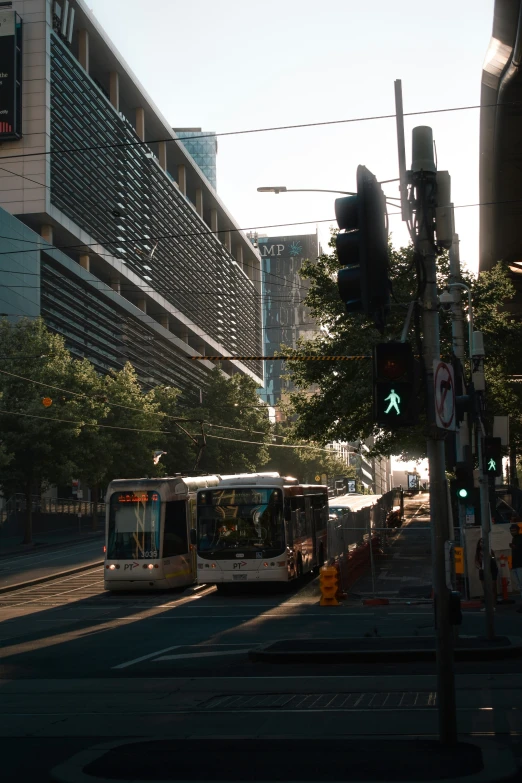 two buses are travelling down the street with tall buildings in the background