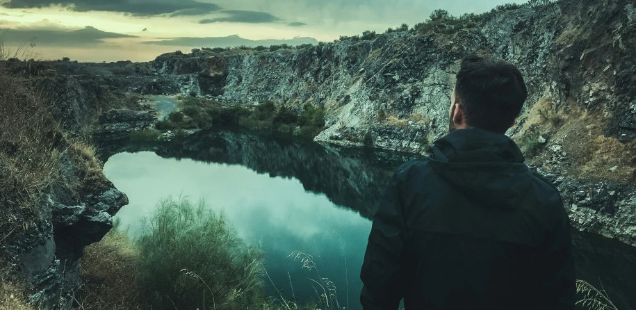 a man is standing on top of a cliff looking at a lake