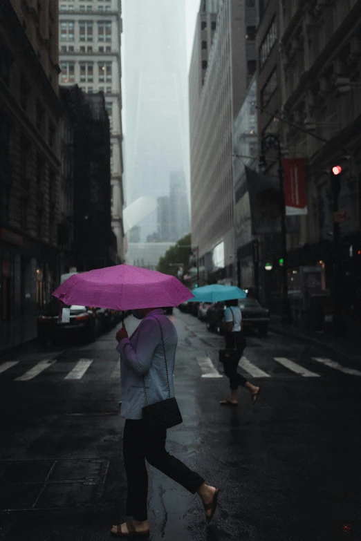 two people walking across a city street with umbrellas