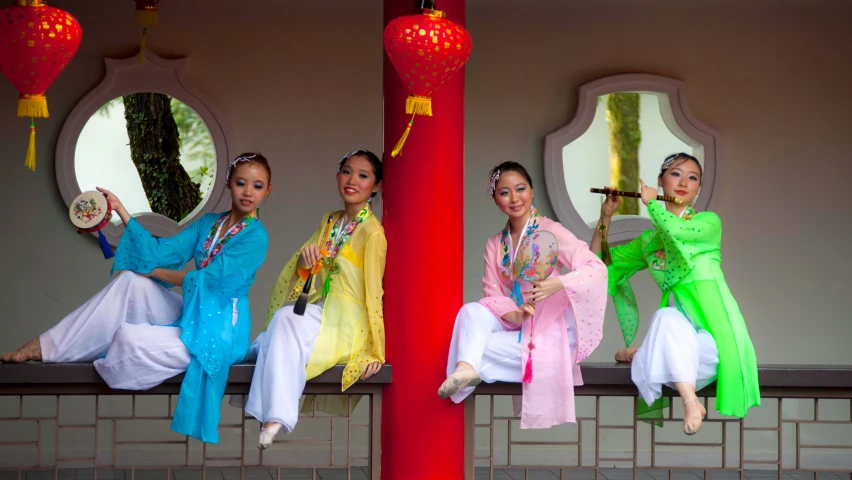 three girls are in traditional colorful costumes with a fan