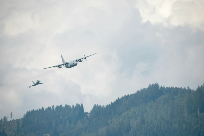 two large planes flying near a hill on a cloudy day