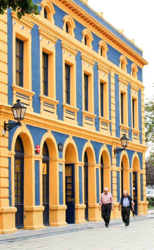 several people are walking past an old blue and yellow building