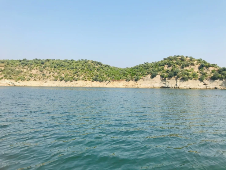 a very blue body of water next to a small island with a forest on the top