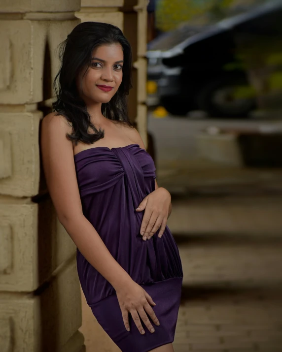 a beautiful young woman in purple dress leaning against a stone wall