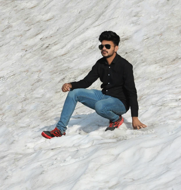 the man is wearing sunglasses and is sitting on a snow bank