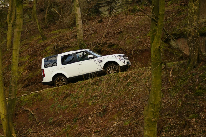 a white suv is sitting on a hill in the woods