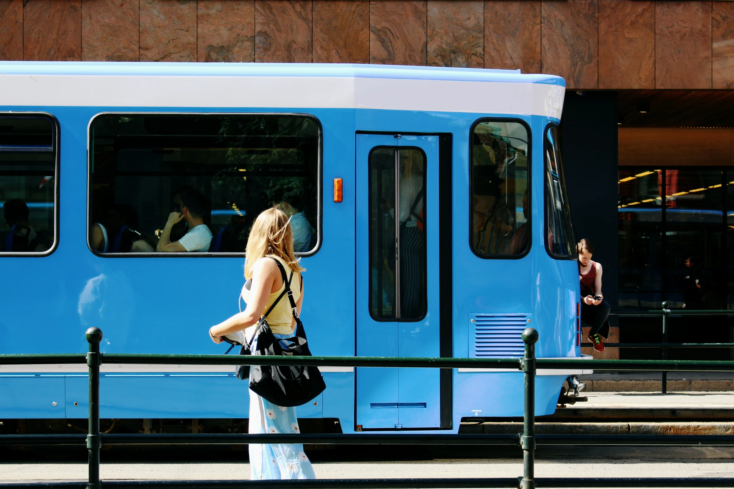 a lady waits at the platform in front of a blue and white bus