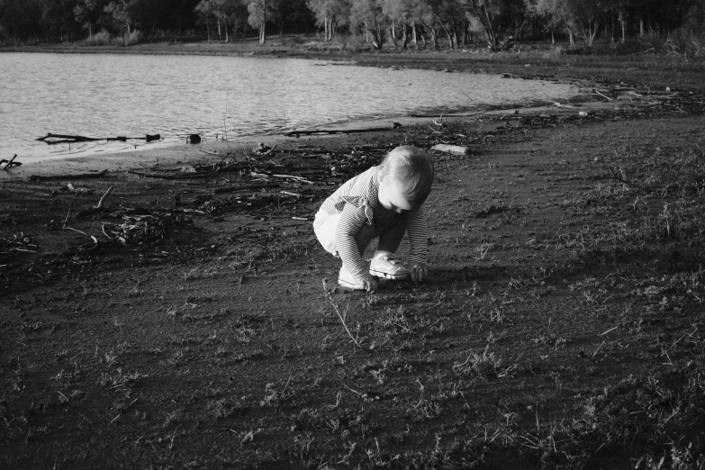 a little boy is crouching in the grass near a lake