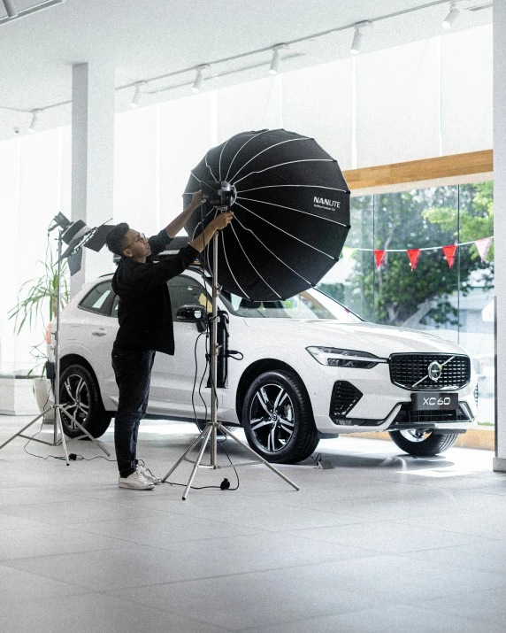 a man in black jacket holding an umbrella standing next to a car