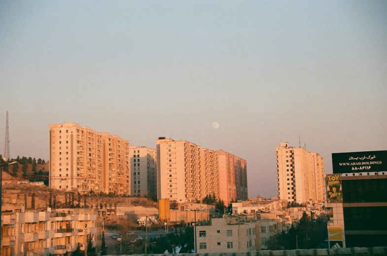 view from a distance of many buildings with the moon in the sky