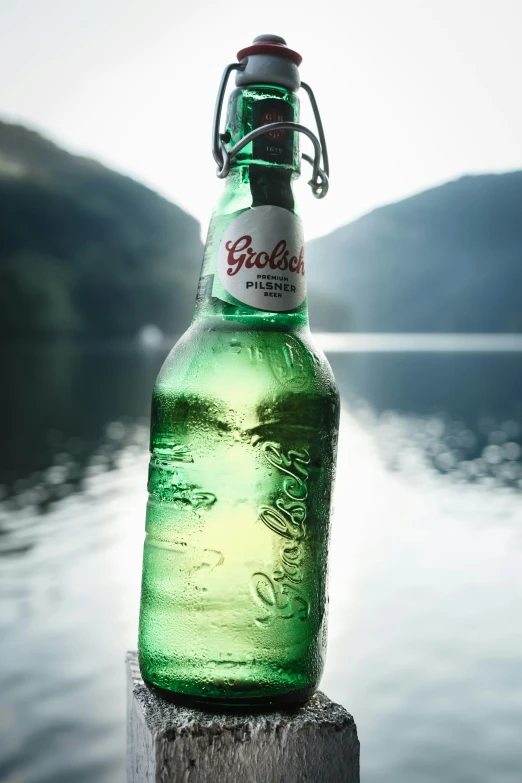 an empty beer bottle sitting on top of a wooden post next to water