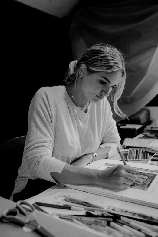 a woman sits at a desk and writes with a pen