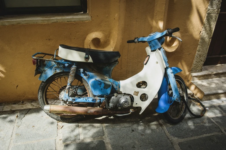 an old, rusted, scooter sits in front of a wall