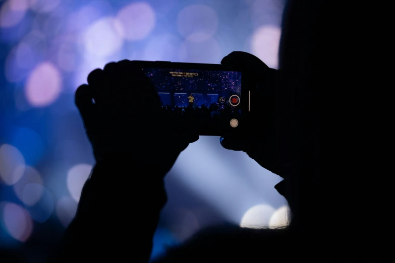 silhouetted person taking a picture of stage from phone