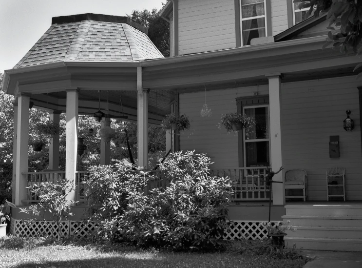 an old - fashioned wooden house has pillars and a gazebo in the foreground