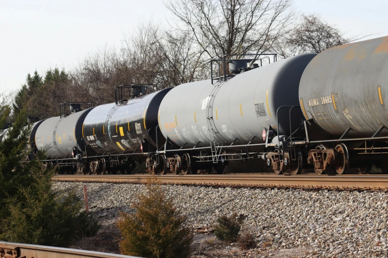 an oil train traveling down tracks next to some trees