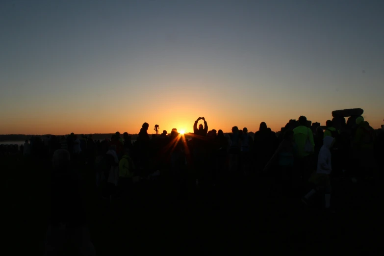 the sun set in the distance with a crowd of people standing around it