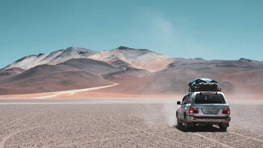 a car with its luggage strapped on top of it sitting in front of mountains