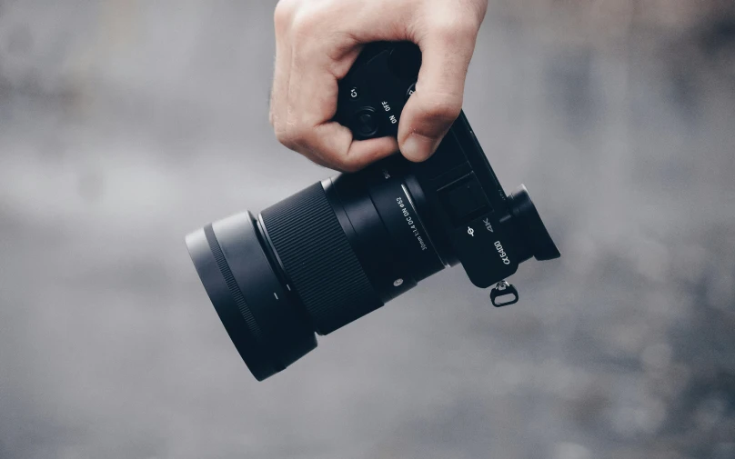 a hand holding a camera over a gray background