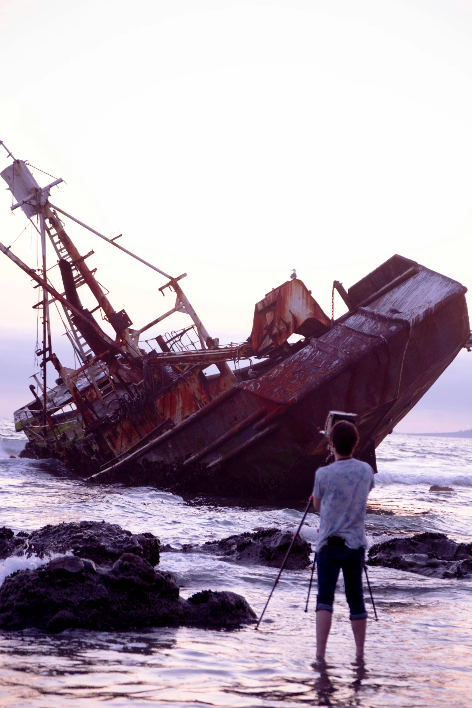 two people standing in shallow water next to an abandoned ship