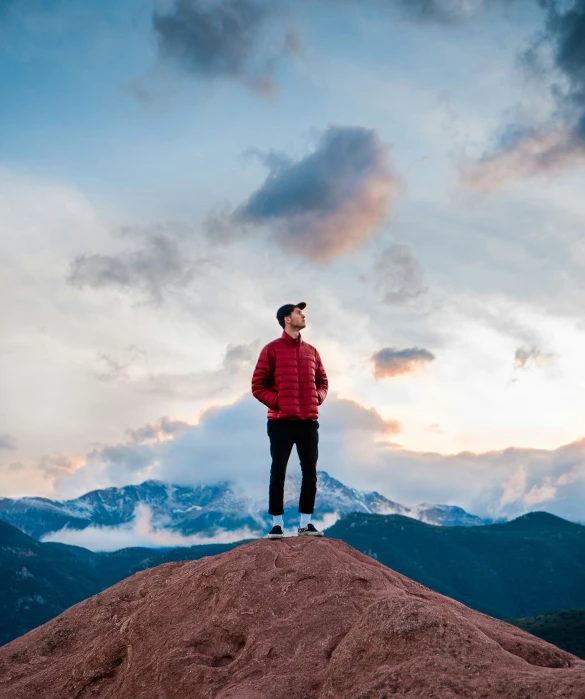 the man standing on top of the mountain is wearing a red jacket