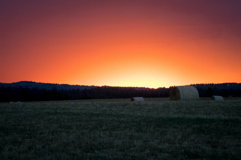 some hay bales in the middle of a field at sunset