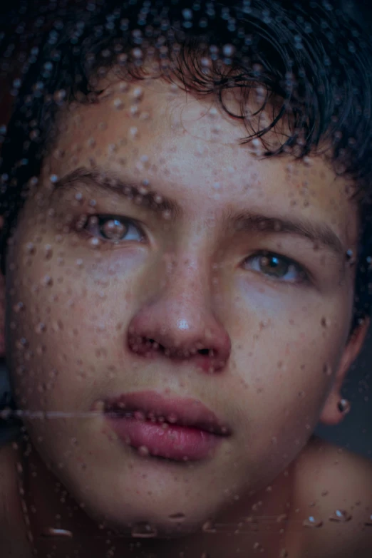 a girl is staring at the camera through a raindrop window