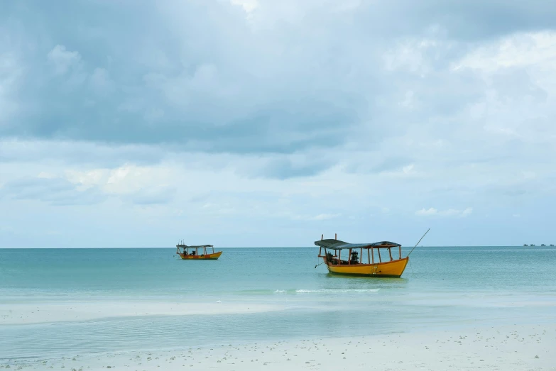 two boats on the shore of the ocean under cloudy skies