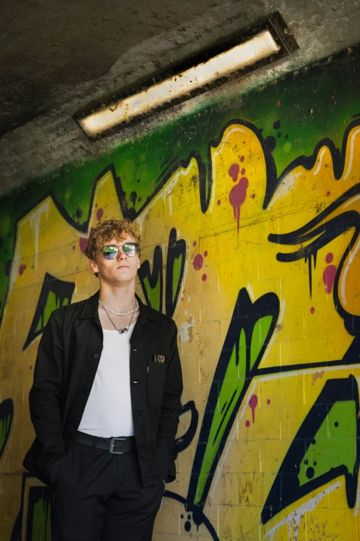 a young man wearing shades in front of a colorful wall