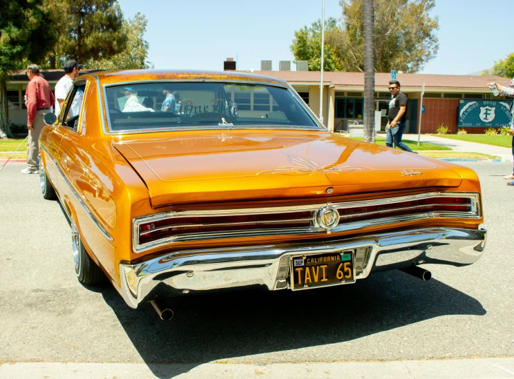 an orange old car sitting in front of people