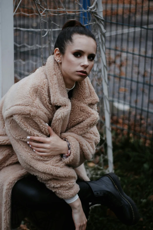 a woman wearing a fur coat next to a fence