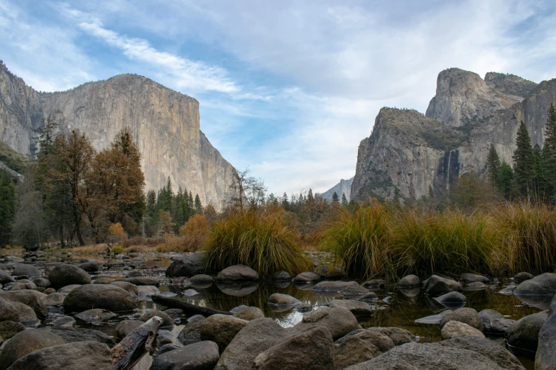 the sky is partly cloudy and there is a small river running between some mountains