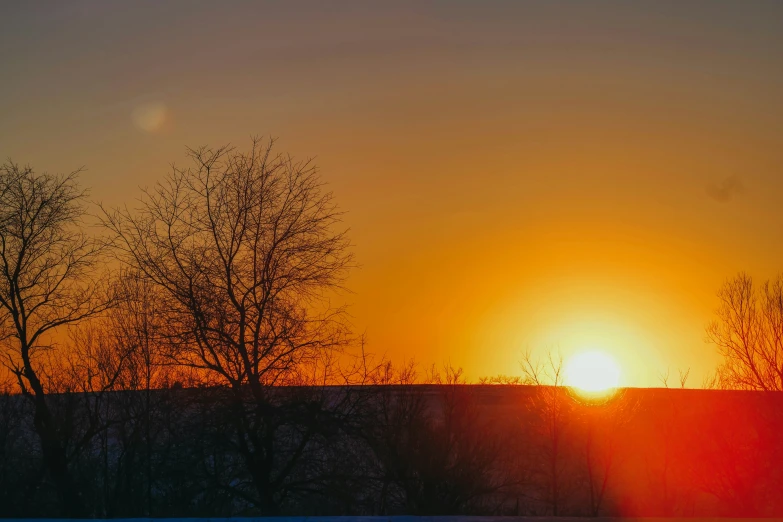 the sun is setting in a field with trees