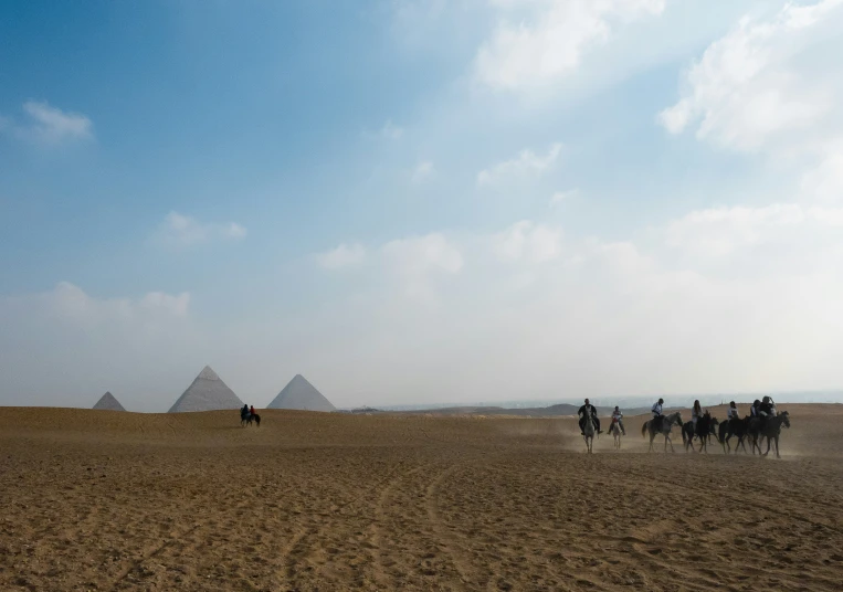 people ride horses through the desert in front of the pyramids