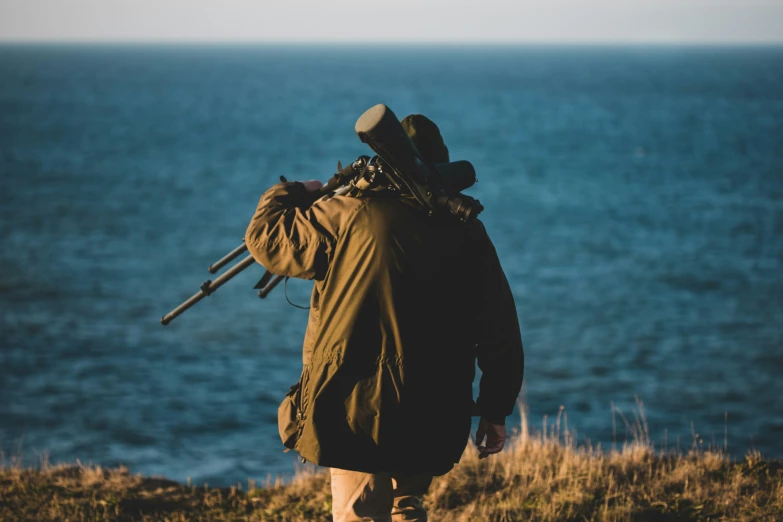 person with backpack and fishing rod on his back standing at the edge of an ocean