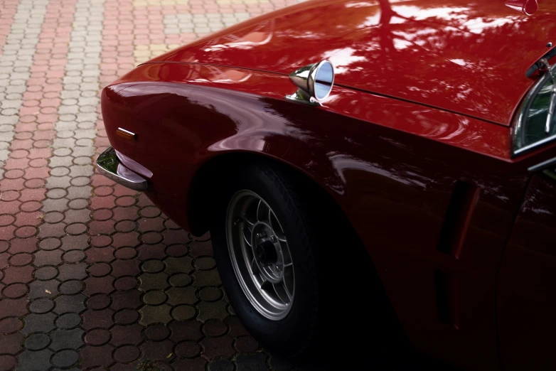 a vintage red sports car parked in front of a brick wall