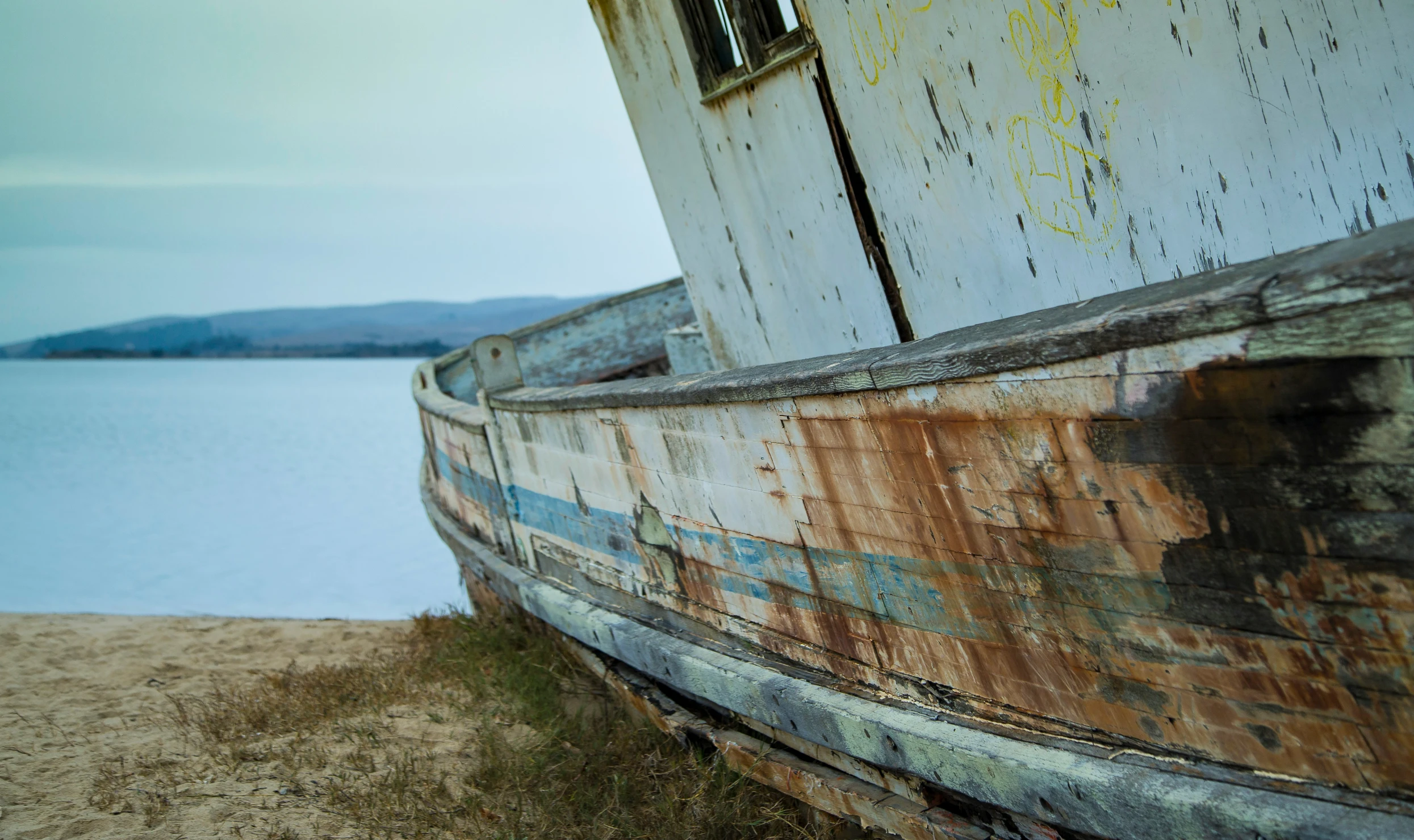 a rundown old boat on the shore of a lake