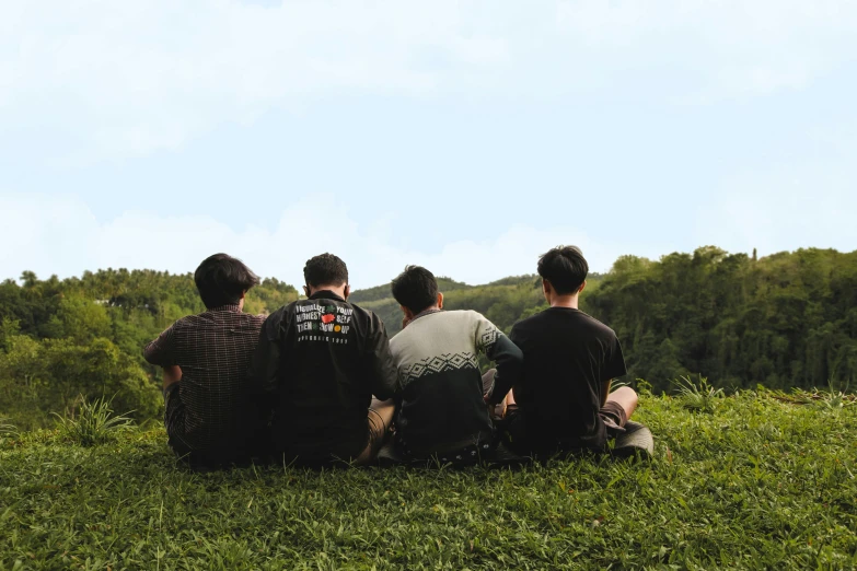 four men are sitting on the grass with a plane in the air