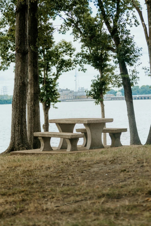 a stone picnic table sits by the water in front of some trees