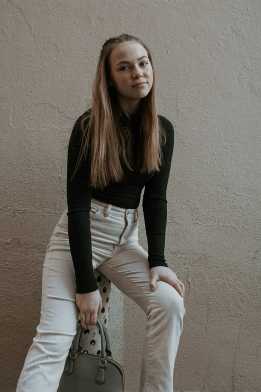 a young woman poses holding a bag near a wall