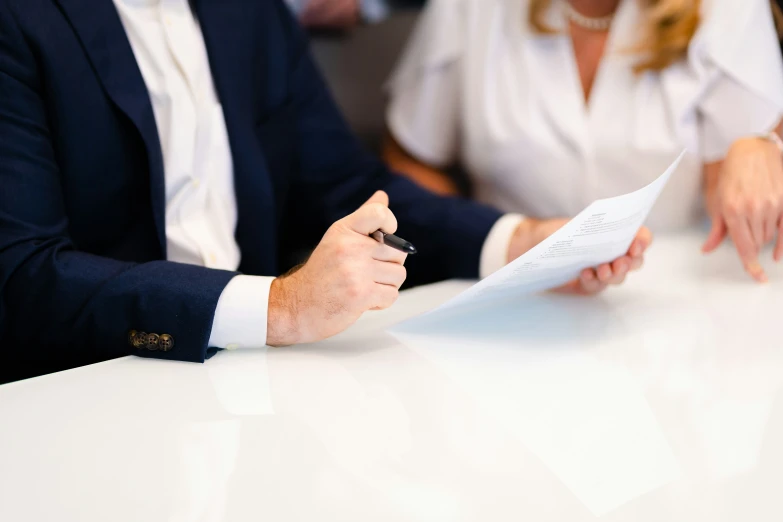 two people are sitting at a white table signing a paper