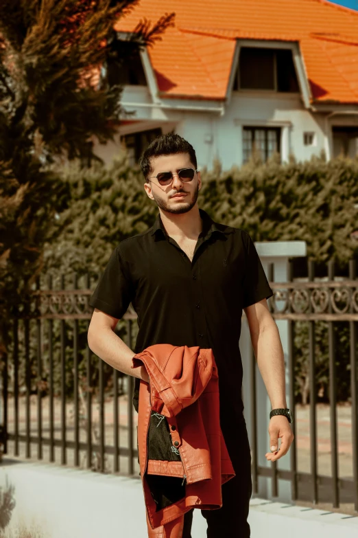 man in sunglasses, black shirt and red pants in front of fence