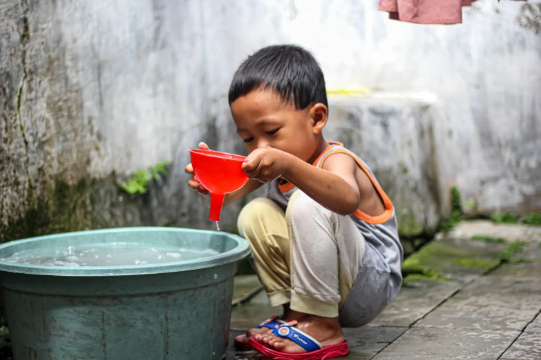 a little boy is sitting by a bucket holding soing