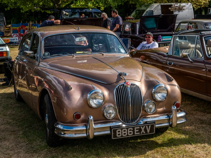 a brown vintage car and an older style car sitting side by side at a car show