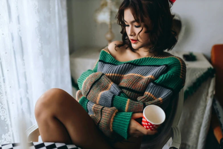 young woman in colorful sweater holding up coffee cup