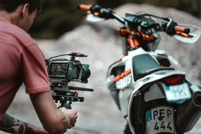 a man holding a camera with his hand out, and another person sitting on a motorcycle