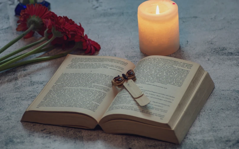 a book with the pages laying on top is open with a candle in front of it