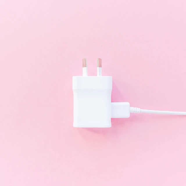 a white electrical plug laying on a pink surface